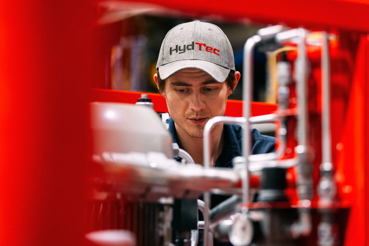 Person wearing a 'HydTec' cap working on machinery with a red foreground