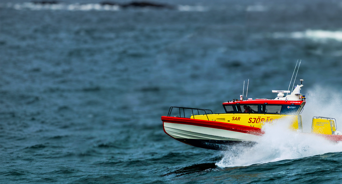 Red and yellow boat speeding on the ocean with visible branding Sjöräddning on the side