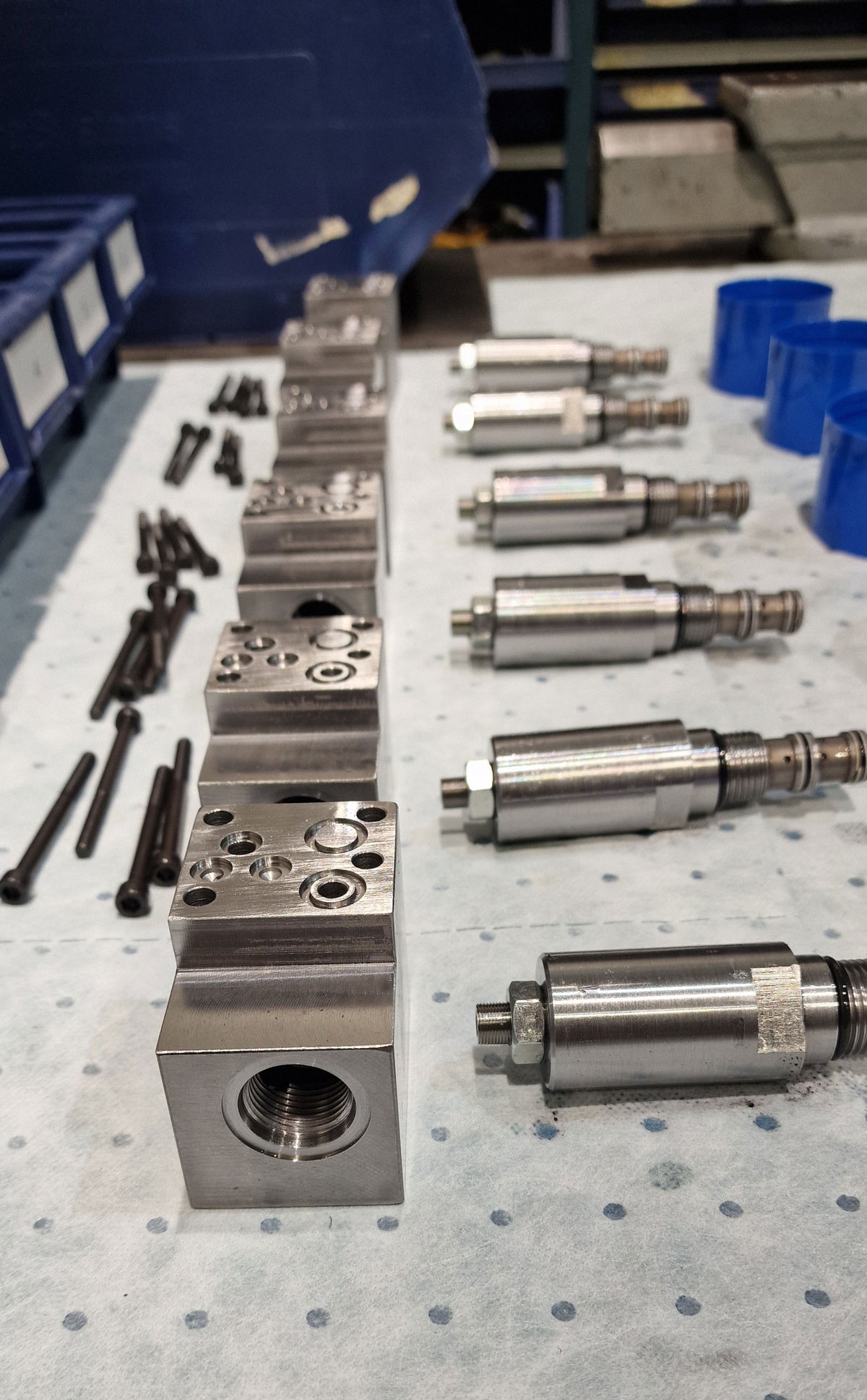 Disassembled V14 manifold hydraulic valve components, including machined valve bodies and cartridge valves with threaded fittings, arranged with mounting bolts before assembly