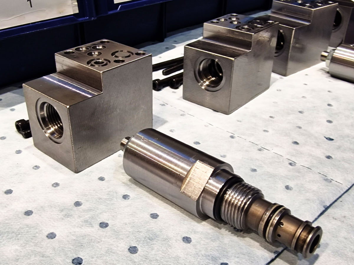 Precision-machined V14 valve bodies with multiple threaded ports, alongside a disassembled cartridge valve showing internal threading and seals