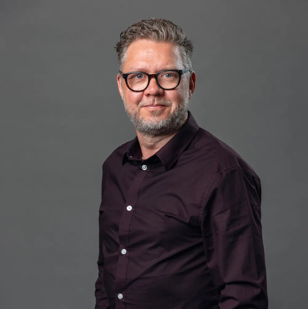Man wearing glasses and a dark shirt against a gray background