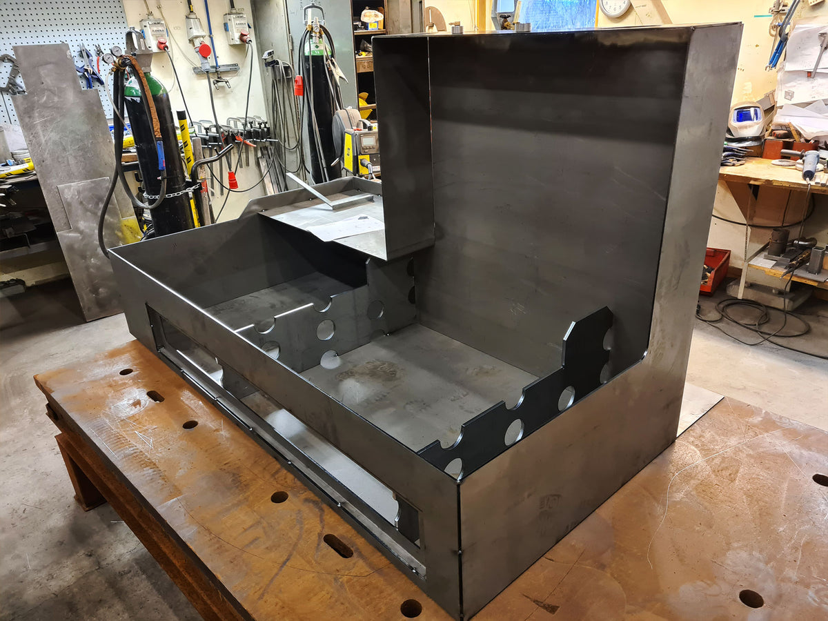 A large custom-built metal cabinet or enclosure made of brushed steel sheet metal, shown on a wooden workbench in a workshop environment.