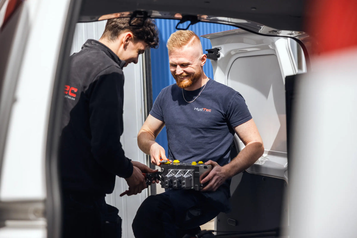 Two HydTec technicians examining a hydraulic valve block together at the back of a service van.