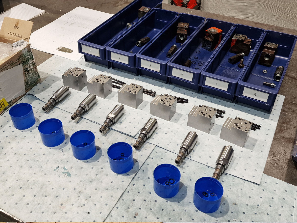 New machined V14 valve components in front, with damaged original parts sorted in numbered bins behind.